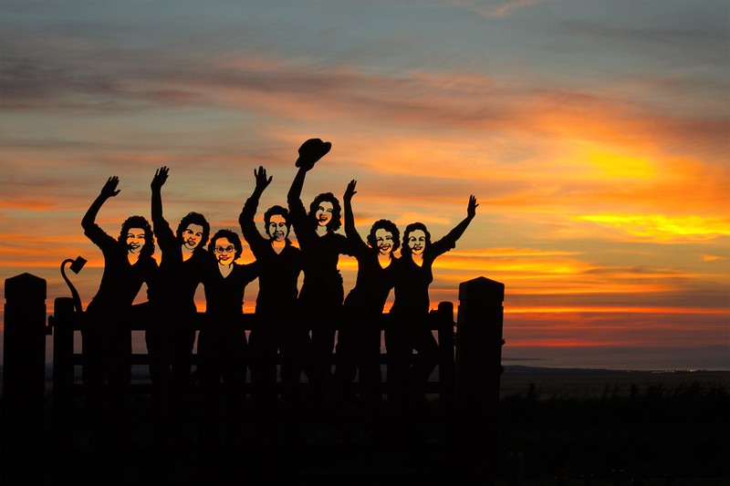 Memorial statue of seven women in silhouette against a sunset