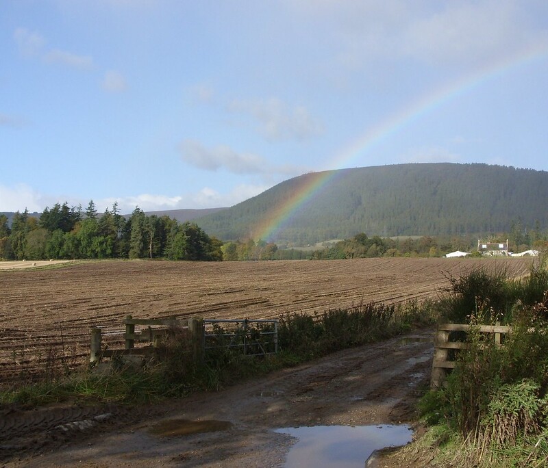Ploughed fields in front of farmhouse and rainbow