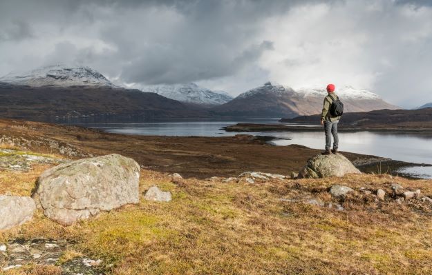 A walker, adventurer looking on to mountains from a stoney shore front.