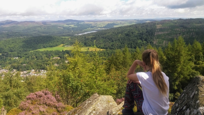Young teenage girl sitting on a hill overlooking Scottish rural landscape