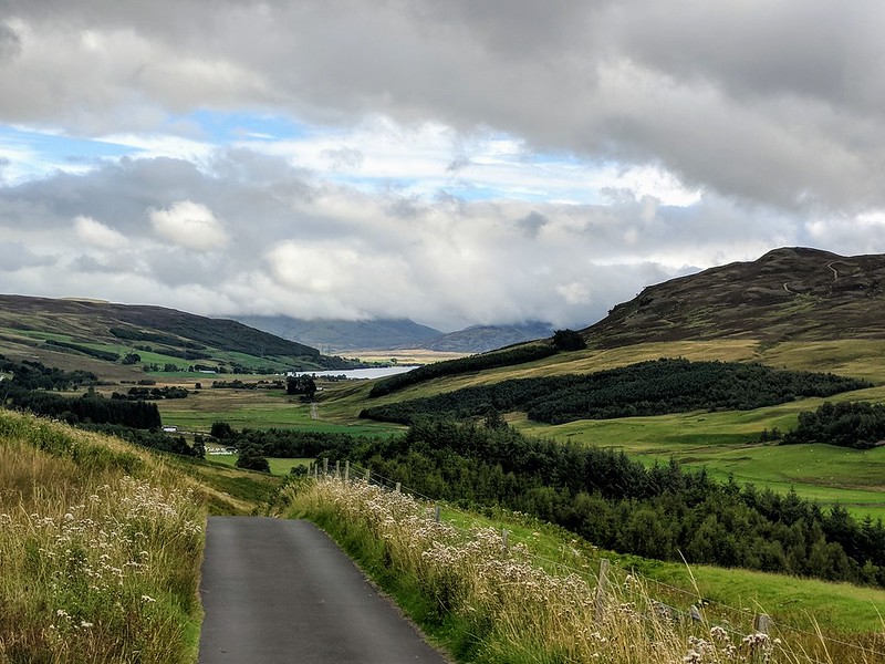 Road running through hills with loch at rear