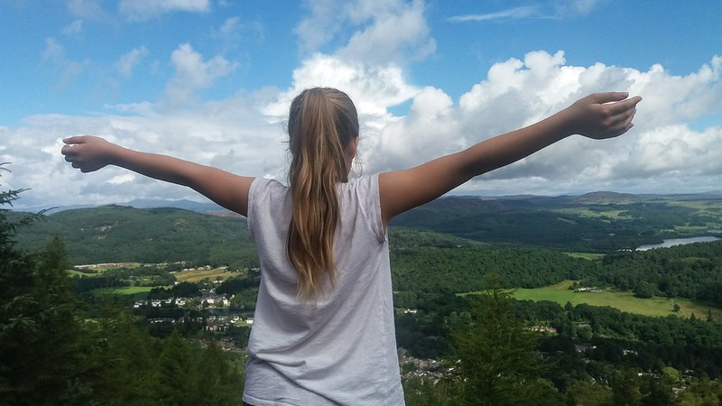Young person, arms wide open to the countryside in the valley below