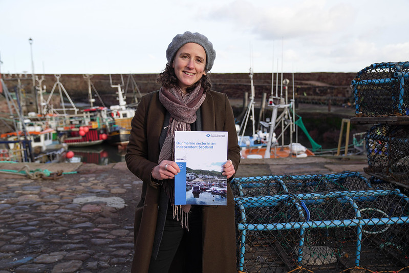 Cabinet Secretary for Rural Affairs, Land Reform and Islands Mairi Gougeon holding document in front of a fishing harbour