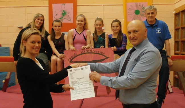 Tom Davis, Chair of the Inner Moray Firth North LEADER Local Area Partnership, presents award to Claire Bath, Chair of Fryish Gymnastics Club with Senior Coach Sonny Rhind and some of the young gymnasts looking on.