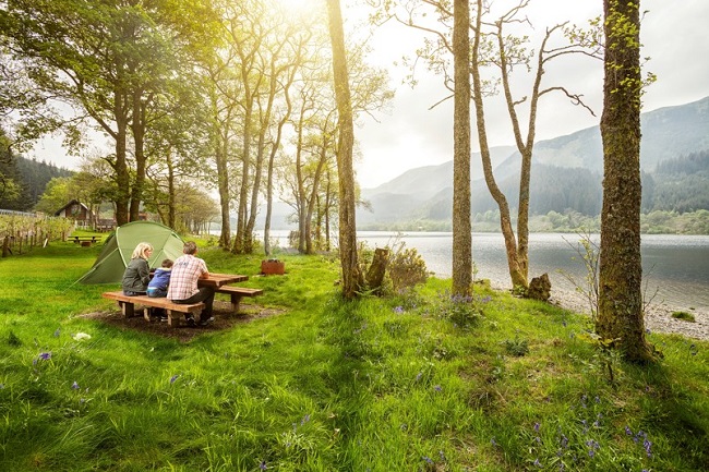 People sitting next on picnic bench next to loch