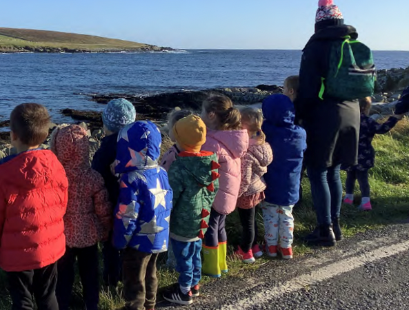Group of children and carer look over a wall at the sea