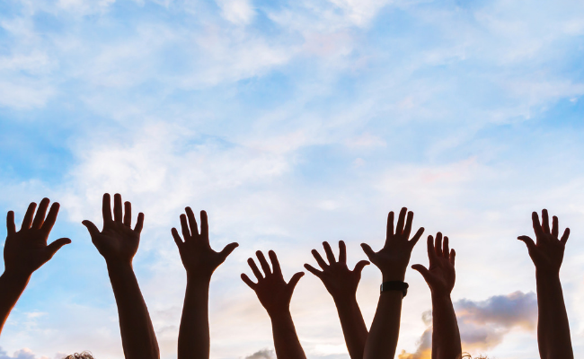 People with hands in the air against blue sky