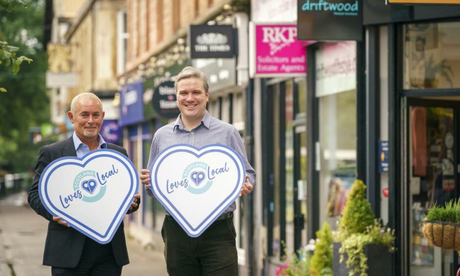 Two men holding Scotland Loves Local badges in street