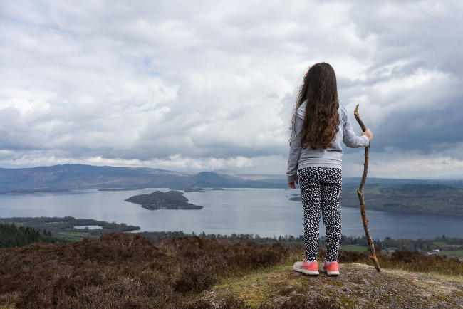 Girl looking out over a Scottish loch from a hilltop