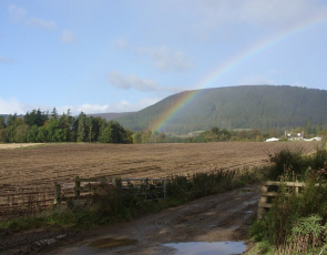 Ploughed fields in front of farmhouse and rainbow