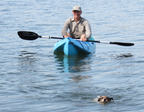 Man in kayak with a dog swimming in front