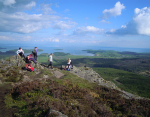 Group of teenagers on hill summit with field and sea views