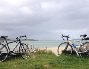 Two bikes on grassy bank overlooking sea and beach 