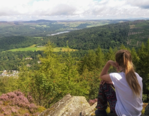 Young teenage girl sitting on a hill overlooking Scottish rural landscape
