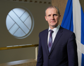 Cabinet Secretary for NHS Recovery, Health and Social Care, Michael Matheson standing in front of a Saltire flag