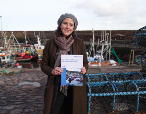 Cabinet Secretary for Rural Affairs, Land Reform and Islands Mairi Gougeon holding document in front of a fishing harbour