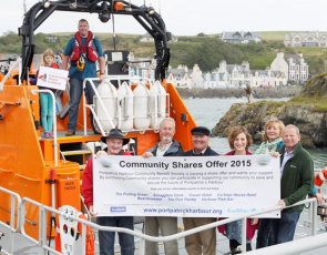 People in lifeboat in harbour with community shares banner
