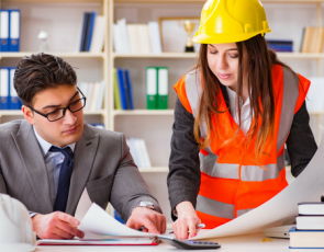 Woman with hard hat speaking to man at desk 