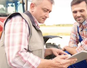 two farmers looking at a tablet beside a tractor