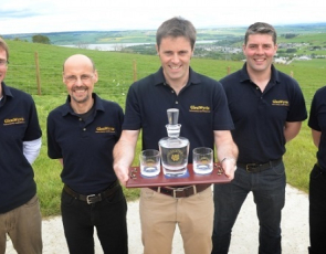 Picture of 5 men holding a whisky decanter and glasses with distilery name engraved on the glassware
