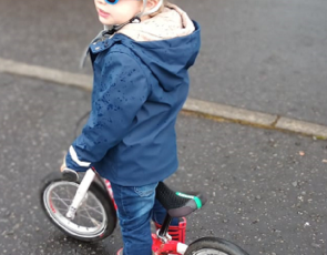toddler wearing blue cycle helmet, sunglasses, on balance bike