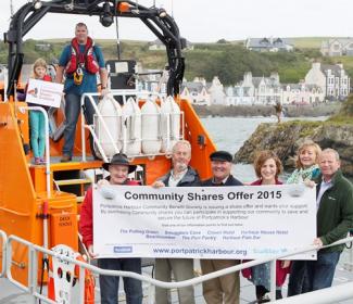 People in lifeboat in harbour with community shares banner