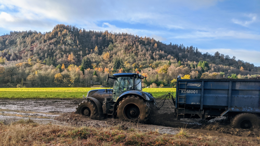 Tractor with trailer driving through muddy field