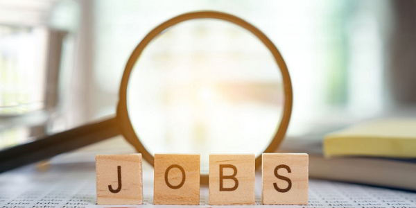 Wooden blocks spelling 'JOBS' with a magnifying glass highlighting the word on a desk.