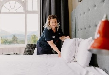 Woman makes up hotel bed in front of arched picture window