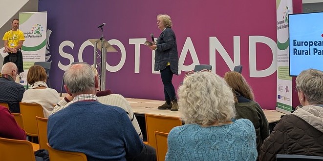 Speaker presenting on stage at the European Rural Parliament event in Scotland, addressing an attentive seated audience.
