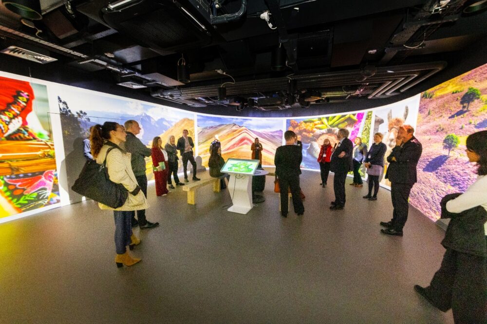 Group of people standing in a circular room with large panoramic nature and cultural images projected on the walls.