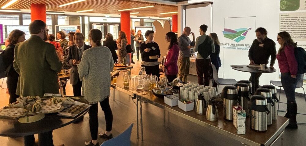 People mingling and enjoying refreshments at a social gathering in a modern indoor space with large windows and red pillars.