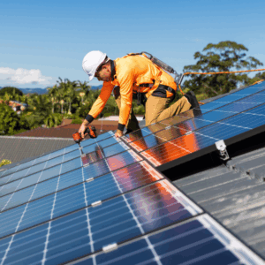 Man in safety gear and hard hat adjusts solar panel on the roof of a building