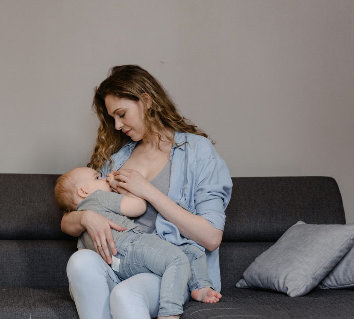 Breastfeeding mum in a denim shirt sitting on a grey sofa 