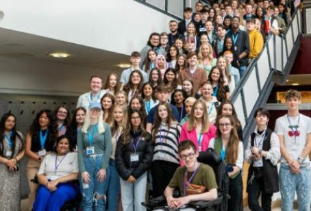 Large diverse group of students gathered on and around a staircase inside a modern school building, smiling for a group photo.