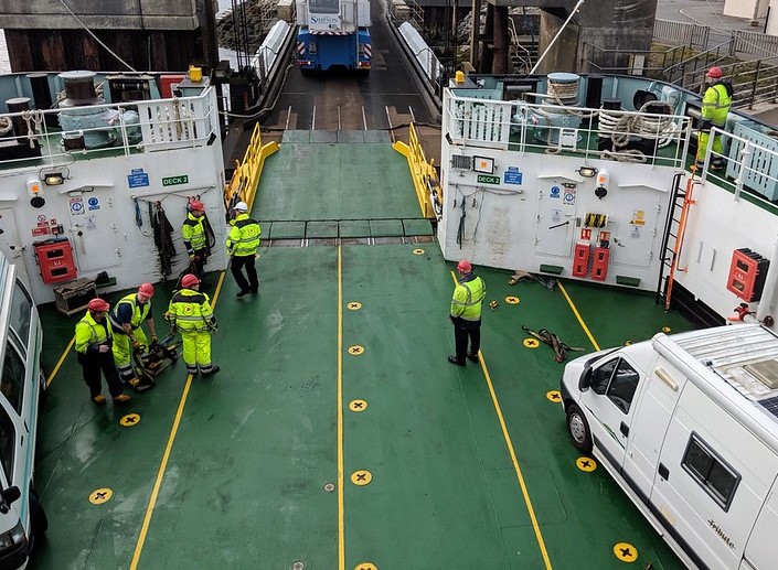 green car deck of a ferry with vehicles and crew