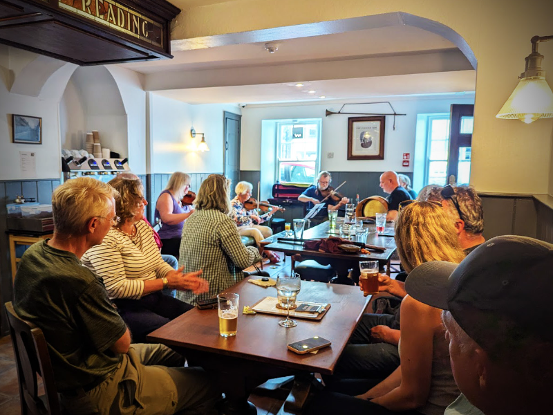 Group of people enjoying live acoustic music in a cosy pub setting with drinks on the table.