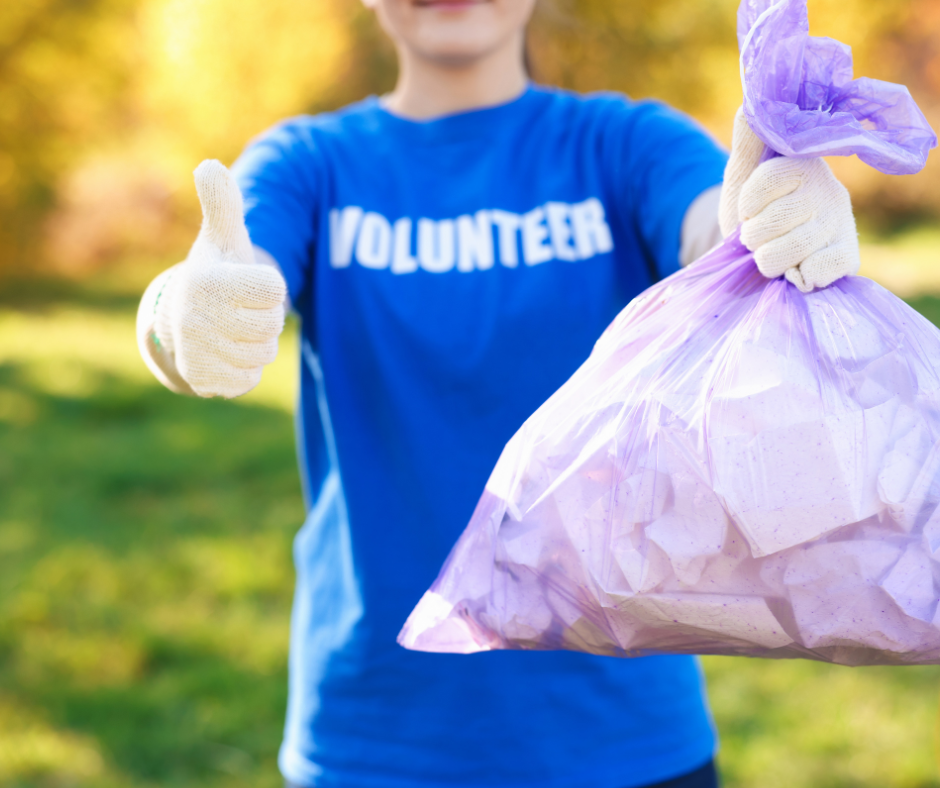 Person wearing blue t shirt with" volunteer" written on it who is holding up a plastic bag