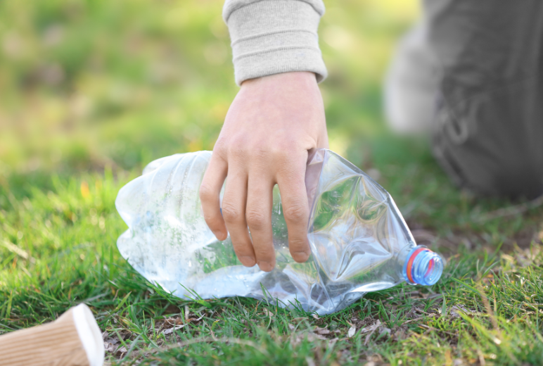 Close up of hand only picking up discarded plastic bottle from grass.