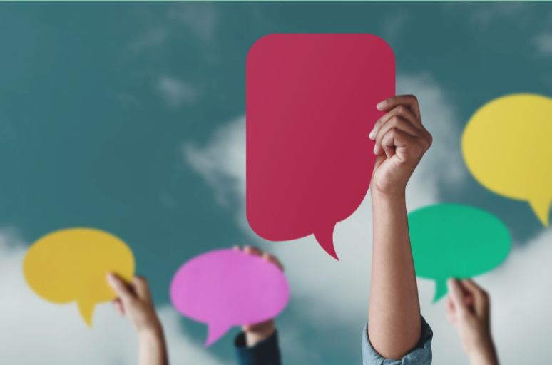 Hands holding colourful speech bubble cut-outs against a cloudy sky background symbolising diverse communication.