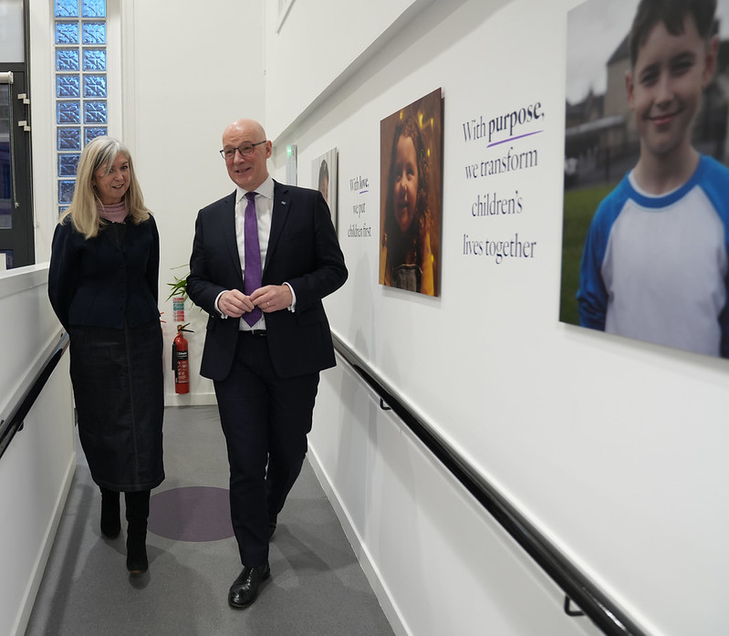 Two professionals walk down a hallway adorned with children's portraits and an inspirational quote about transforming children's lives.