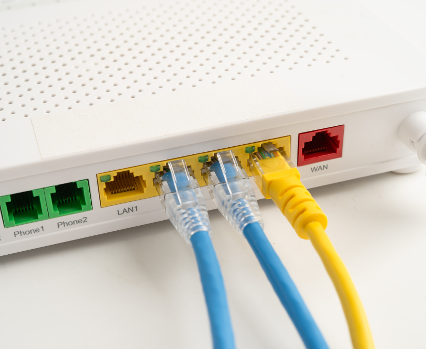 Close-up of a white router with two blue Ethernet cables connected to LAN ports and a yellow cable plugged into the WAN port.