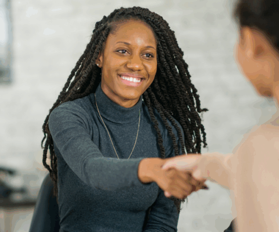 Woman in dark gey clothing reaching out to shake hands with another person