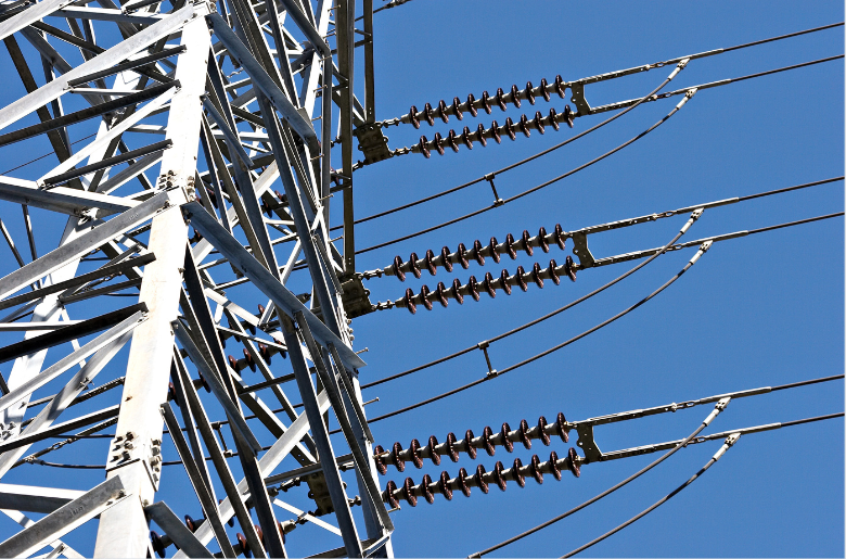 Close-up of a metal electrical transmission pylon with insulators and power lines against a clear blue sky.