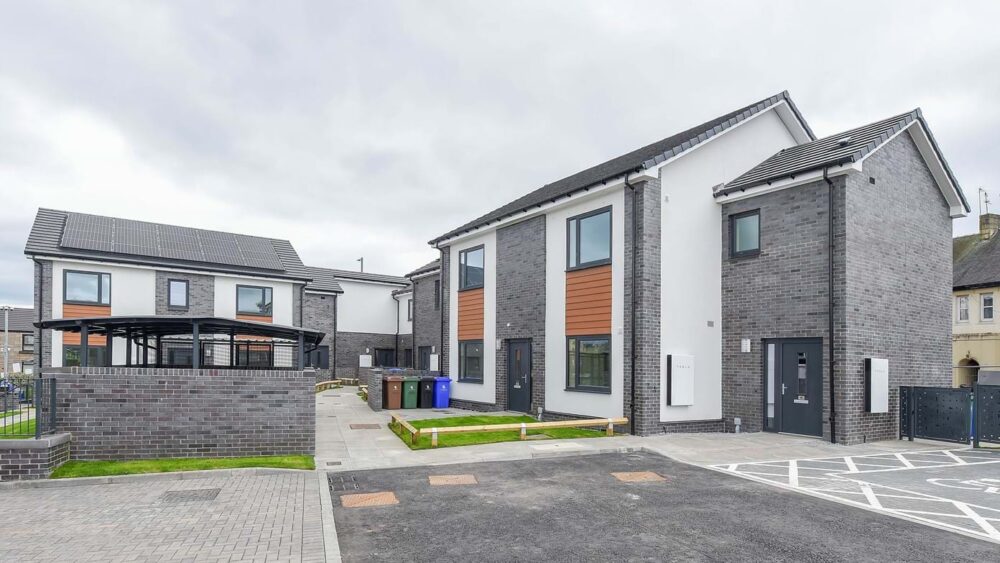 Modern two-story residential buildings with grey brick and white walls under a cloudy sky.