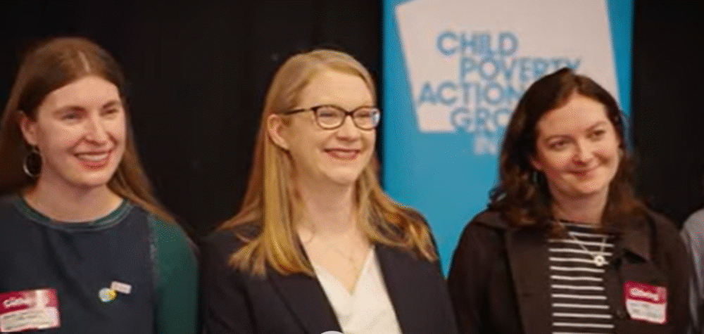 Three women seated in front of a blue banner reading 'Child Poverty Action Group' during an event.