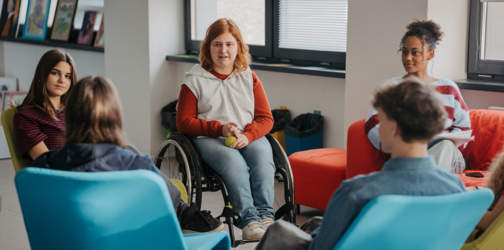 A diverse group of young adults sitting in a circle, engaged in a discussion in a bright room with modern furniture.