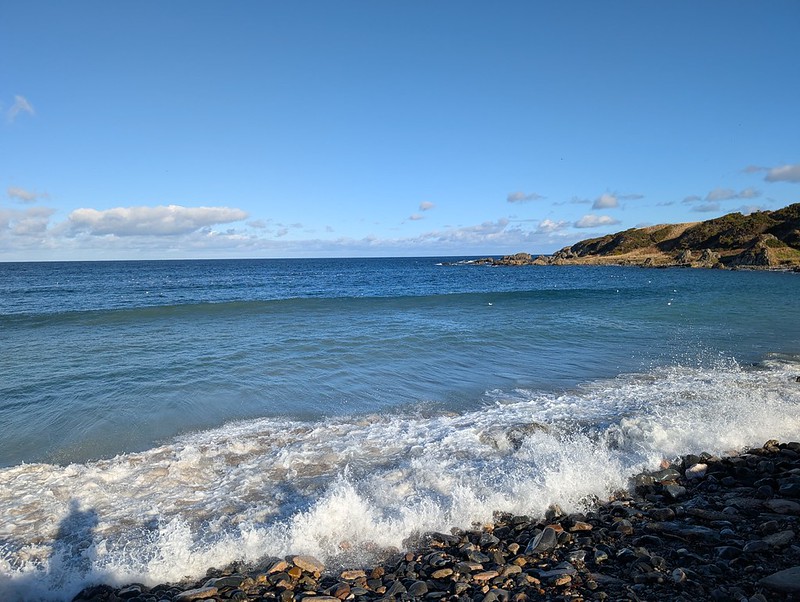 White waves breaking on a shingle beach under a blue sky