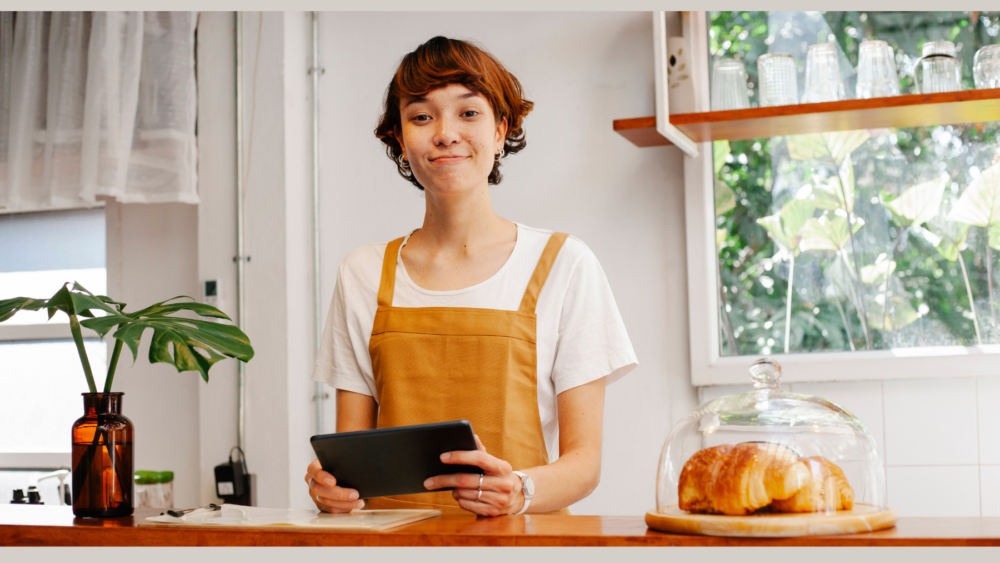 Smiling employee with tablet at counter in bakery