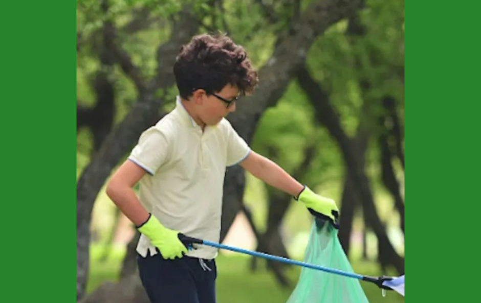 young person in a light coloured top and dark trousers picking up litter in a wooded area using a grabber and wearing gloves